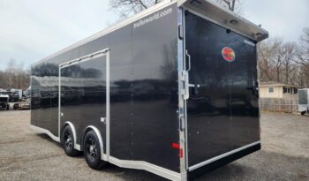 Large black enclosed cargo trailer with dual axles and chrome wheels, parked on a gravel lot; trailerworld.com visible on the top edge of the trailer edge.