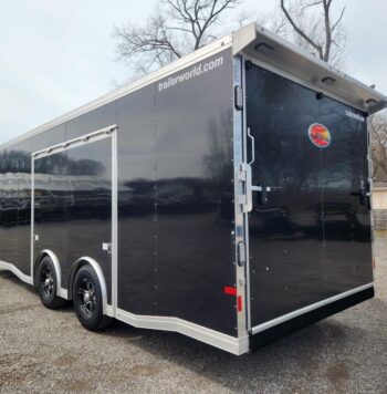 Large black enclosed cargo trailer with dual axles and chrome wheels, parked on a gravel lot; trailerworld.com visible on the top edge of the trailer edge.