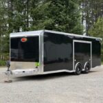 Black enclosed two-axle cargo trailer on a gravel lot with trees in the background.