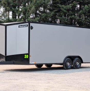 Enclosed gray cargo trailer with black trim and Haulmark branding, a tandem axle, parked on a gravel lot.